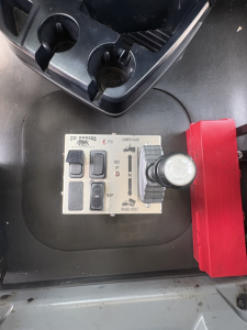 Panel with switches and levers labeled OFF/ON, LOWER HOIST, TARP, and DUST DOOR? plus a red actuator on right. Visible text includes LOWER HOIST, TARP, UP/DOWN arrows, and circular power/selector switch.