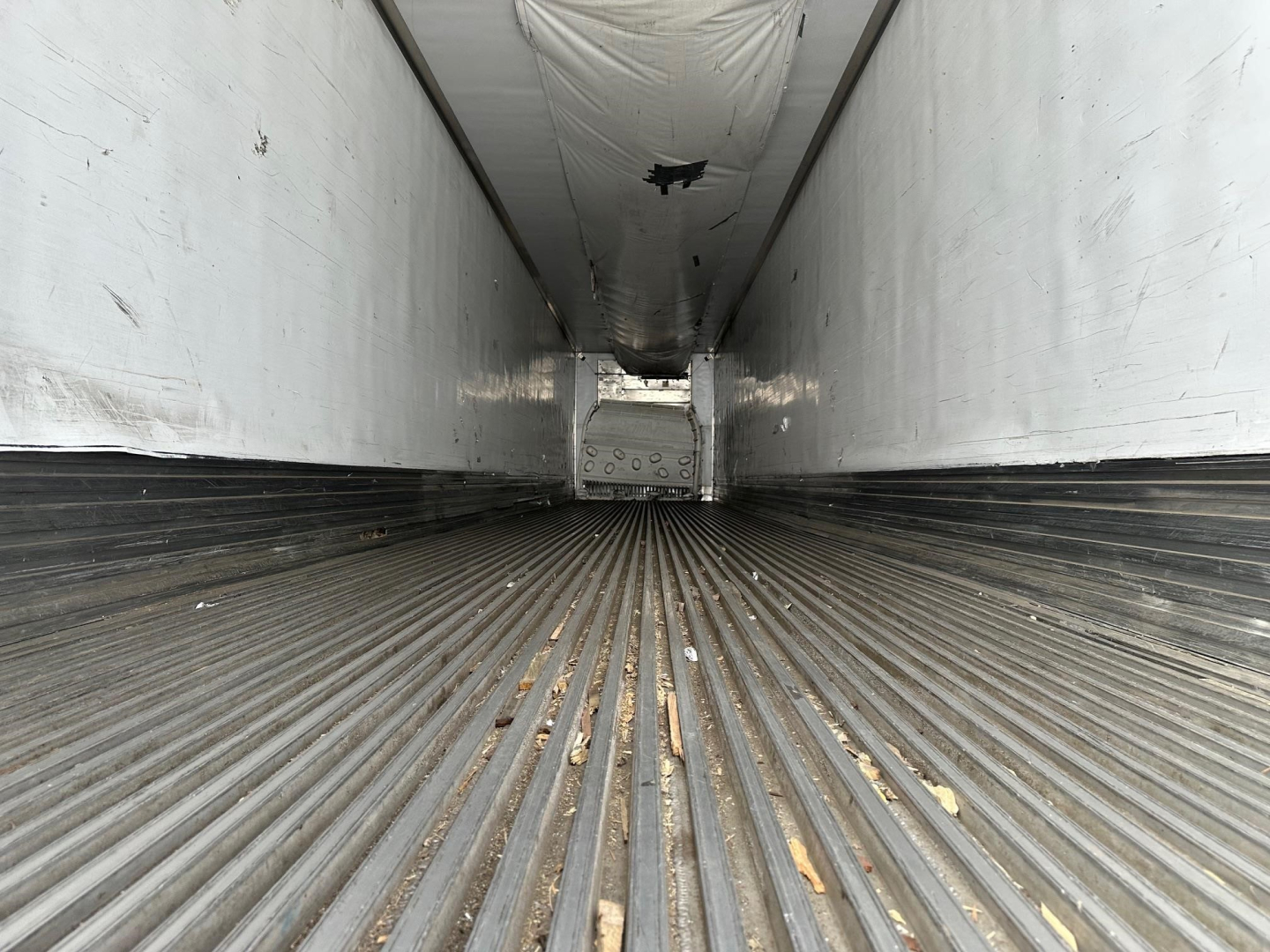 Trailer interior showing ribbed metal floor and white walls; long loading bay with open end and rear door structure visible.