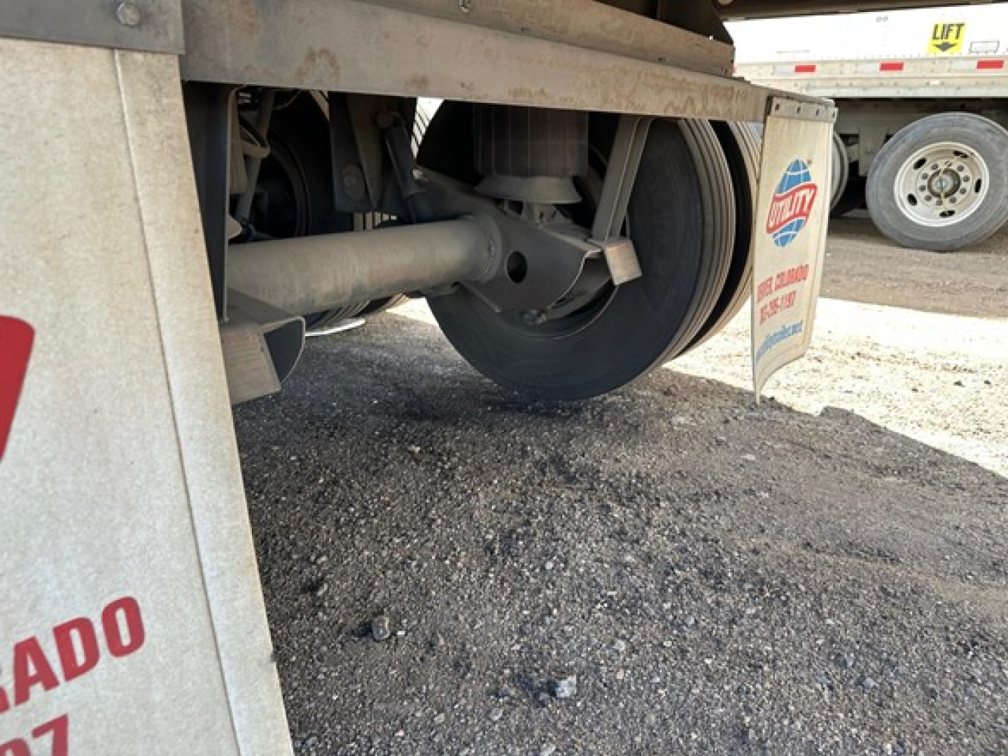 Trailer undercarriage showing wheel hub and suspension for a Utility 3000R trailer, with mud flaps and gravel ground.