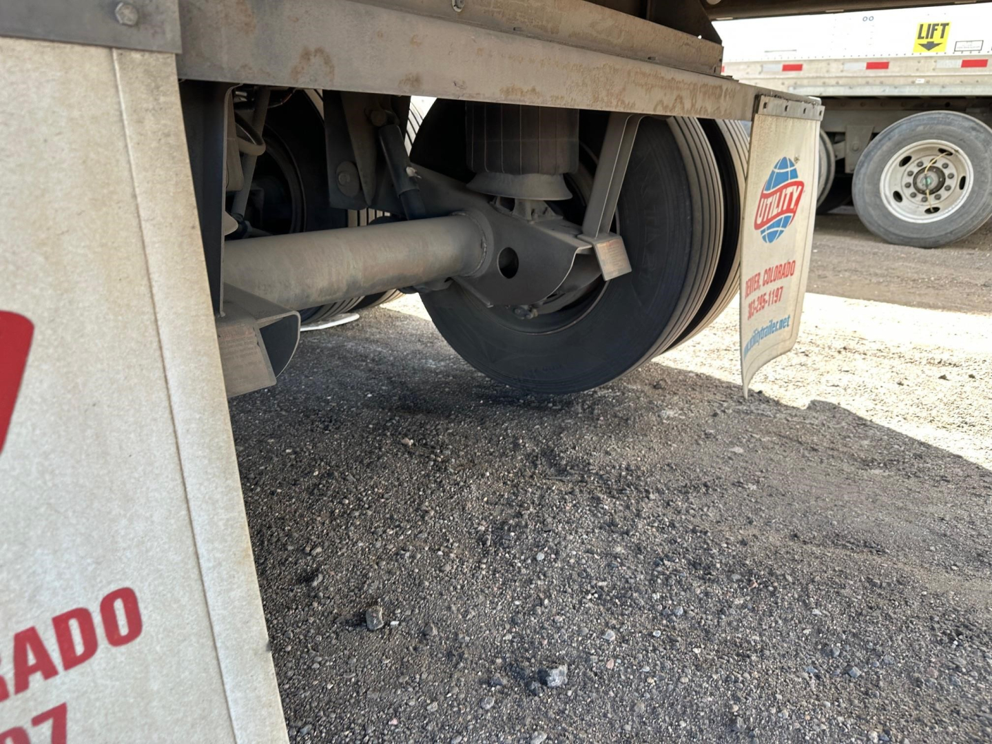 Trailer undercarriage showing wheel, axle, suspension components, and mudflap with utility logo.