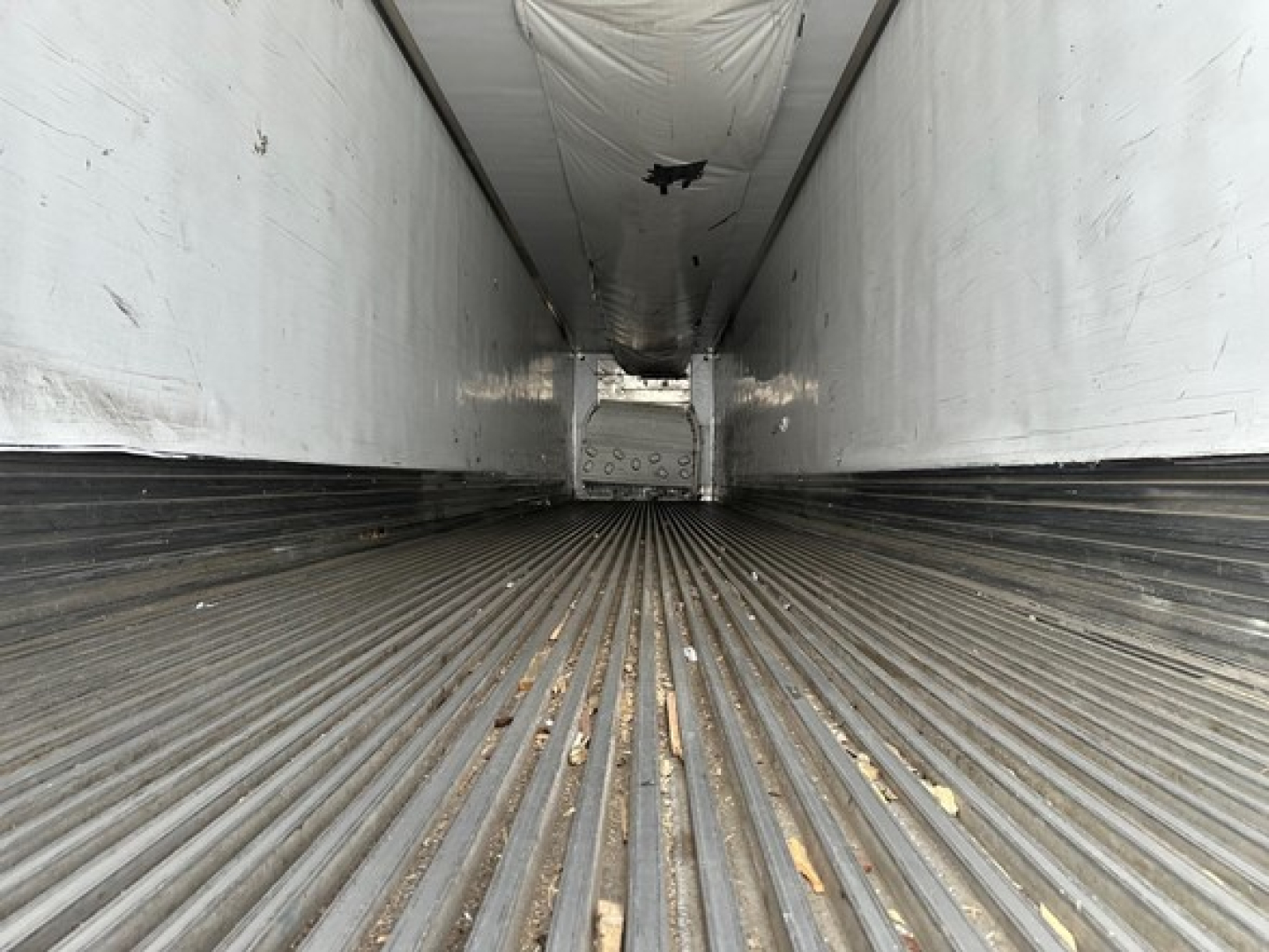 Interior of a Utility trailer showing ribbed metal floor and white side walls; perspective from rear toward front with light at far end.