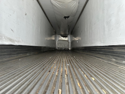Trailer interior showing ribbed metal floor and white walls; long loading bay with open end and rear door structure visible.