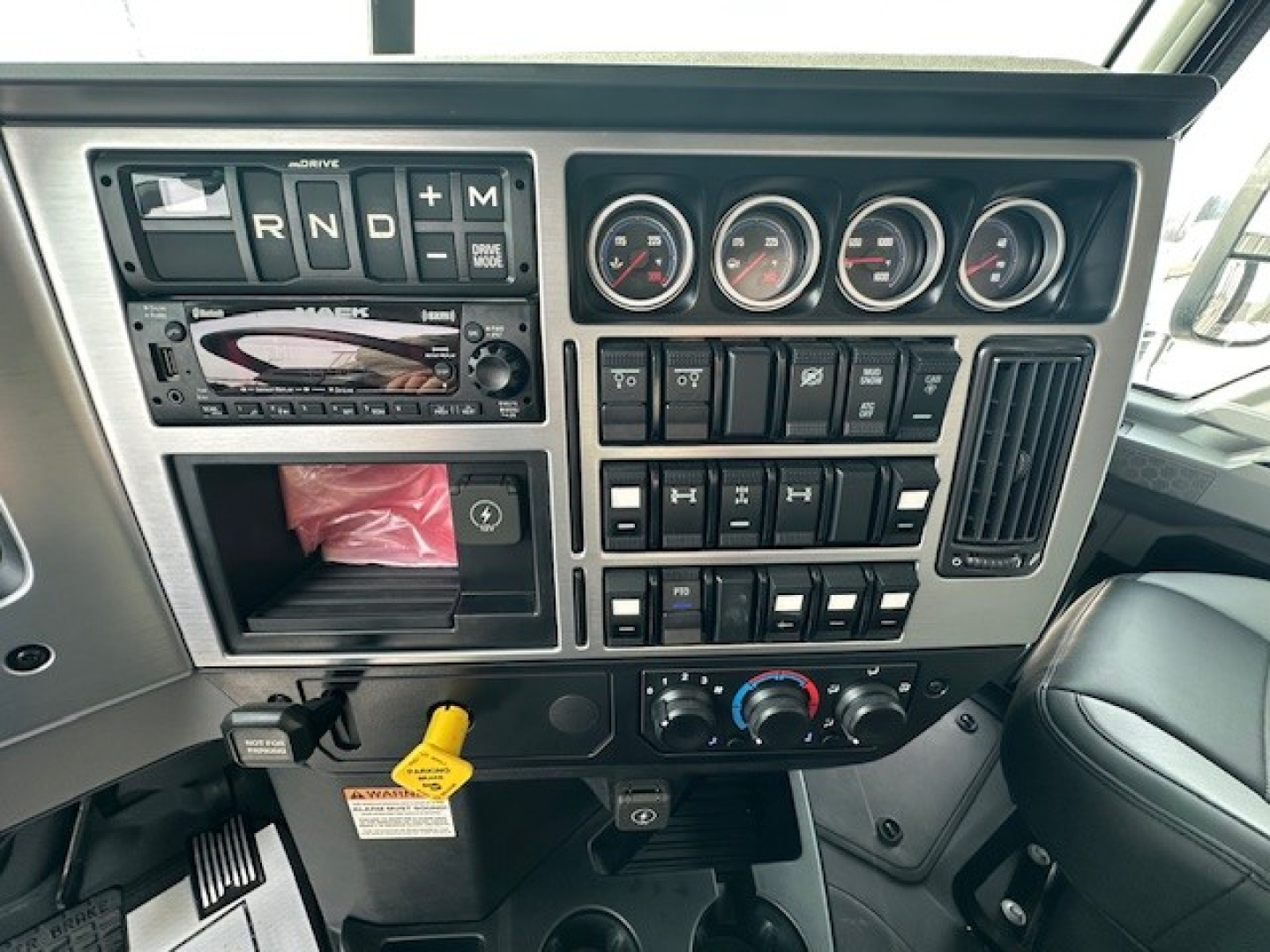 Dashboard interior of a Mack truck showing gear selector R N D P and a touchscreen stereo, several gauges, switches, and climate controls.