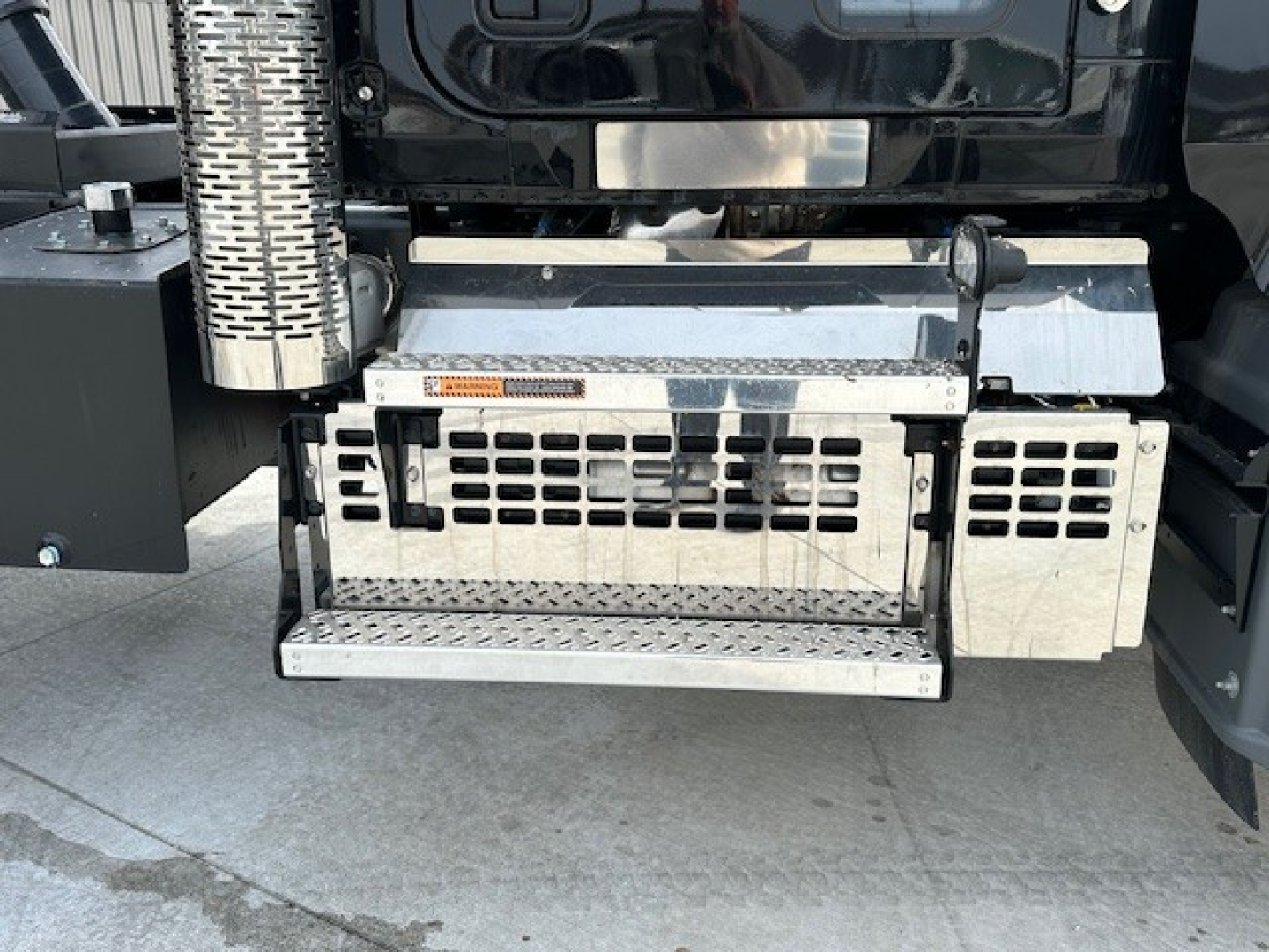 Truck side step and underbody area of a 2025 Mack GR104F dump truck showing metal steps, perforated vents, and hydraulic components.