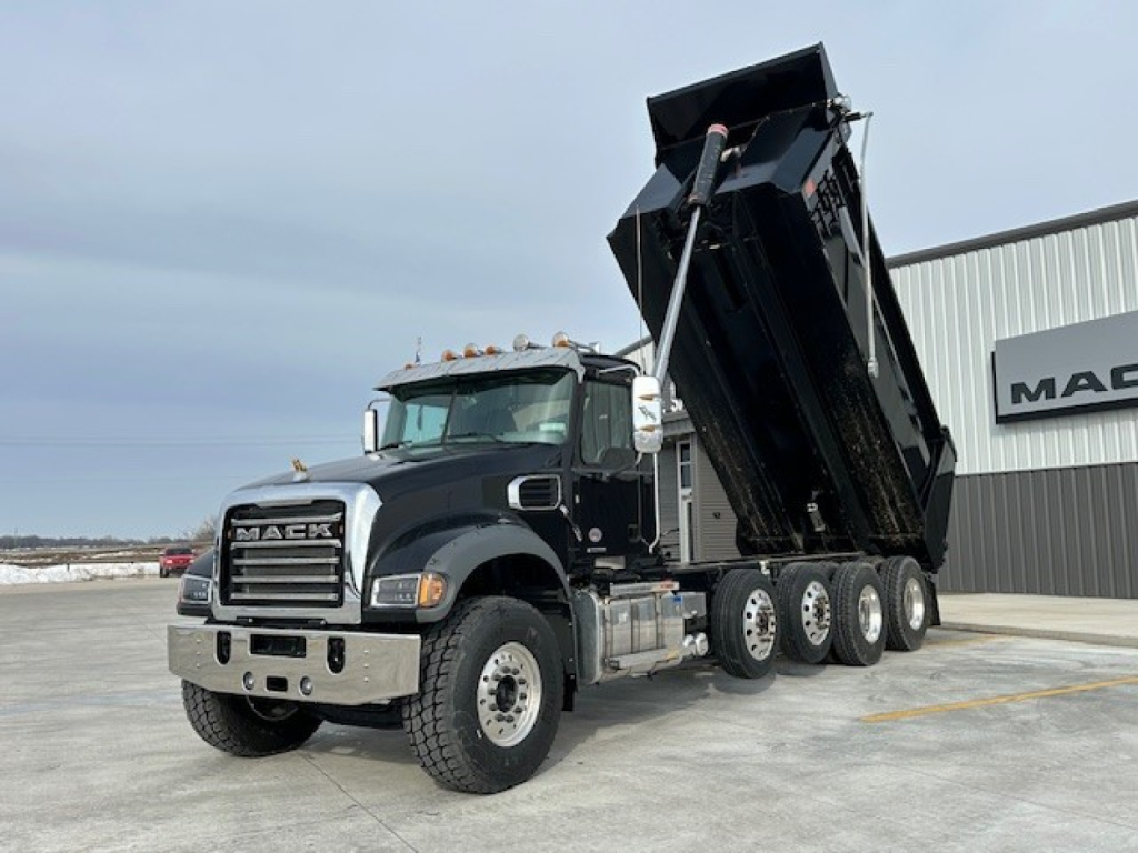 Mack GR104F dump truck with raised dump bed in a dealership yard, front grille and Mack logo visible