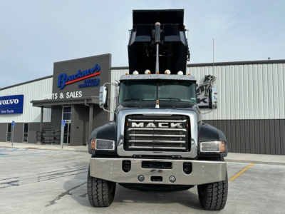 Dump truck front view showing Mack grille, headlights, chrome bumper, and raised dump bed in a dealership lot.