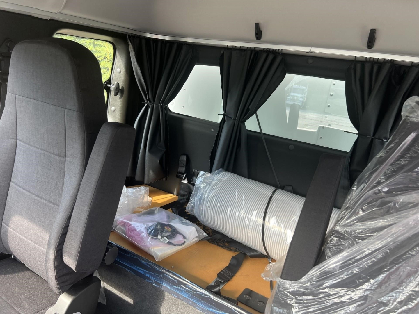 Freightliner M2 106 Plus cab interior showing seats and cargo area with plastic-wrapped items and partition curtains.
