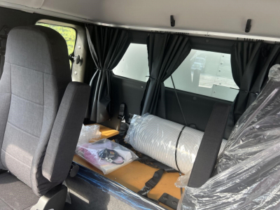 Freightliner M2 106 Plus cab interior showing seats and cargo area with plastic-wrapped items and partition curtains.
