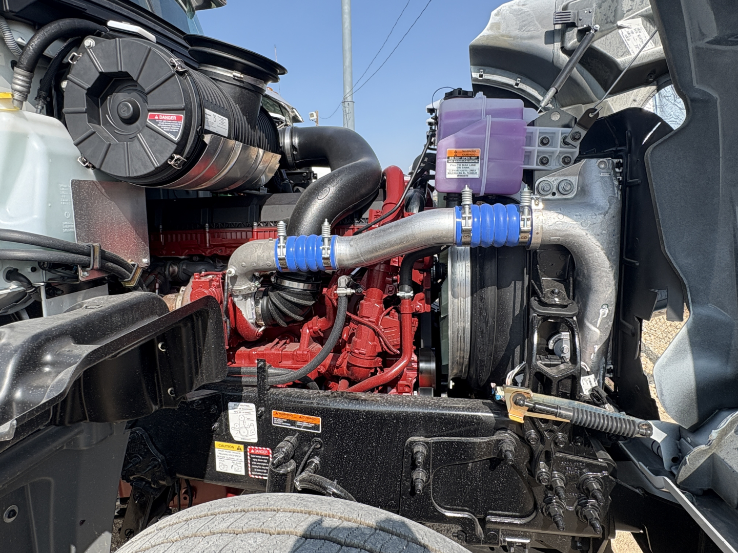 Mack GR64FT engine bay showing turbo charger, coolant reservoir, hoses, and purple coolant surge tank.