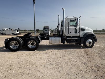 Side view of a white Mack GR64FT conventional daycab truck chassis showing dual rear axles, fuel tank, and exhaust stacks.