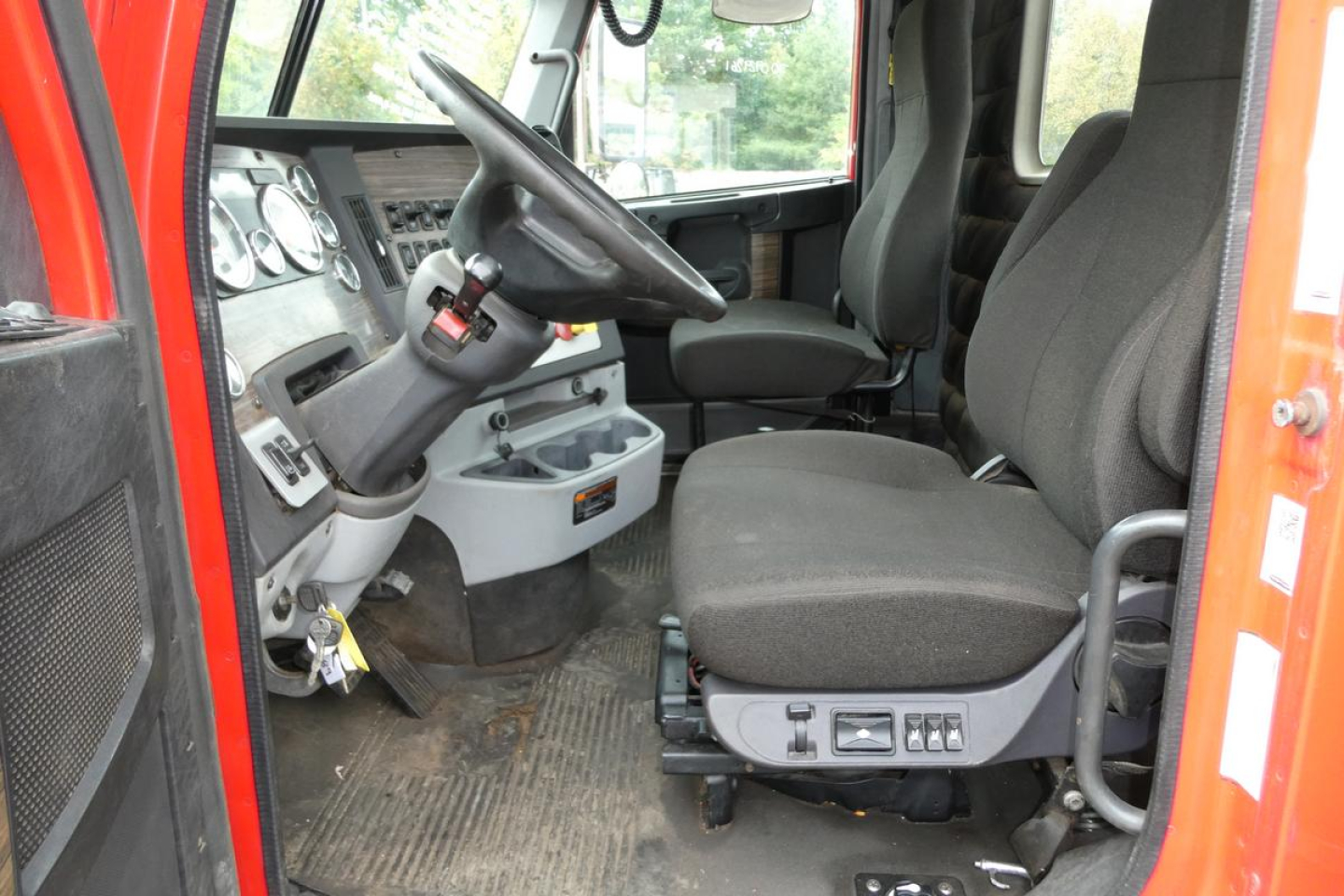 Truck cab interior of a 2019 Freightliner SD122 showing the driver's seat, steering wheel, and dashboard with various gauges and controls.