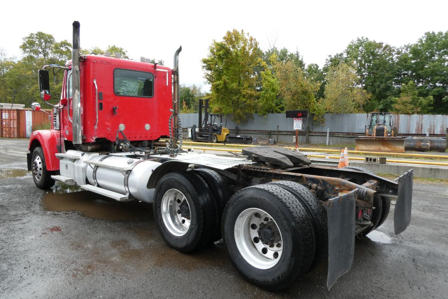 Freightliner SD122 truck chassis in red cab with dual rear axles and fifth wheel, side view showing exposed drivetrain and rear tires.