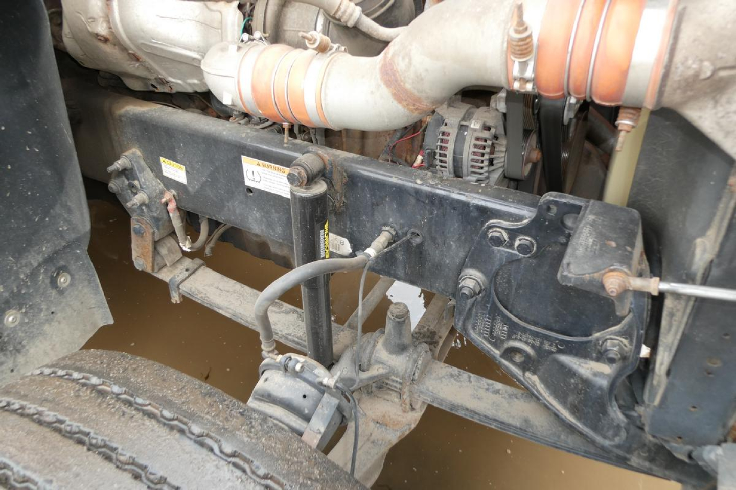 Conventional daycab truck chassis showing frame, suspension, and engine components with hoses and belts in view.