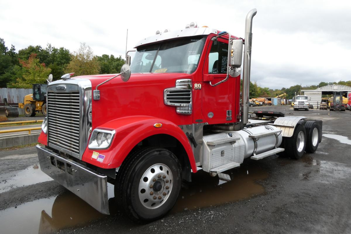 Freightliner SD122 conventional daycab tractor showing red cab, chrome grille, twin vertical exhaust stacks, front bumper, dual rear axles, and large fuel tanks.