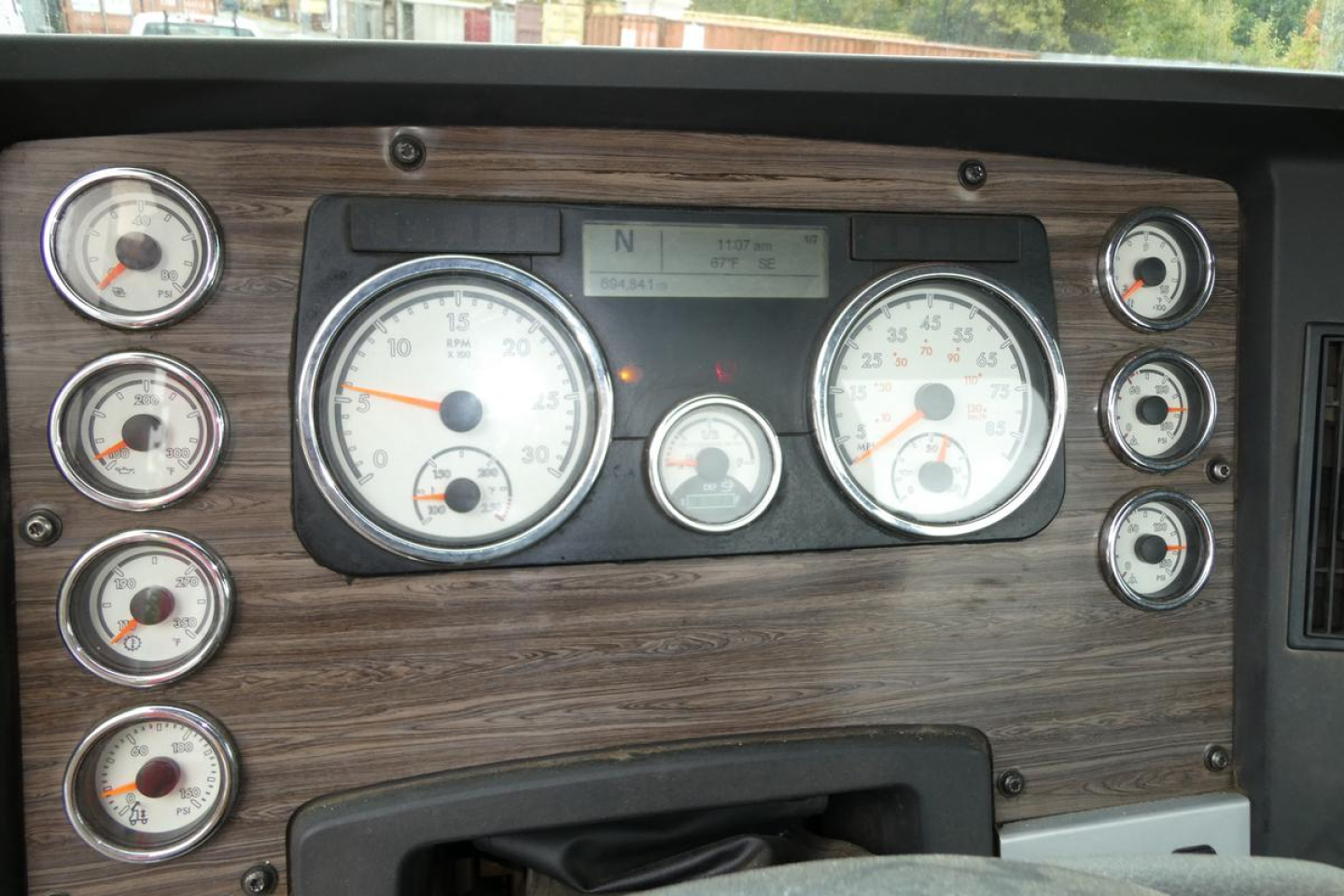 Dashboard panel of a Freightliner SD122 truck showing multiple gauges and woodgrain dash veneer.