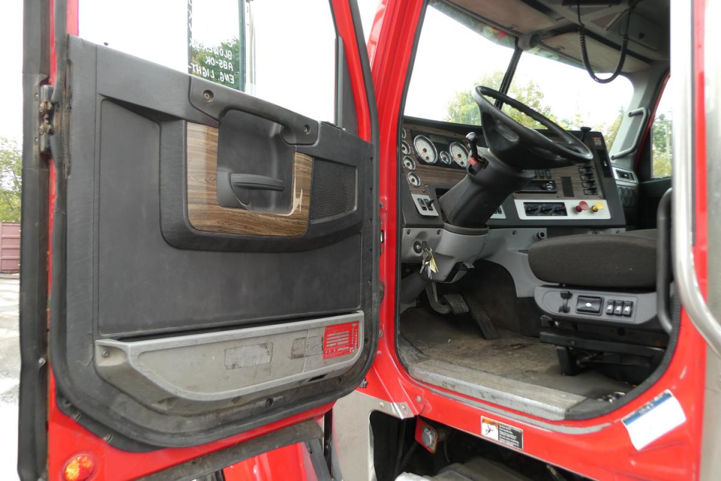 Cab interior of a 2019 Freightliner SD122 truck with driver’s door open, showing steering wheel, dashboard, and entry area.
