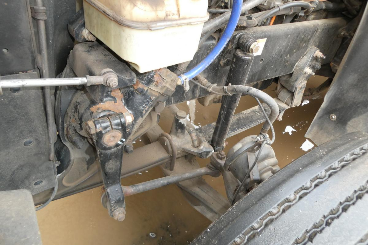 Conventional daycab Freightliner SD122 engine bay showing hydraulic hose, steering linkage, brake components, and a blue hose near the brake reservoir.