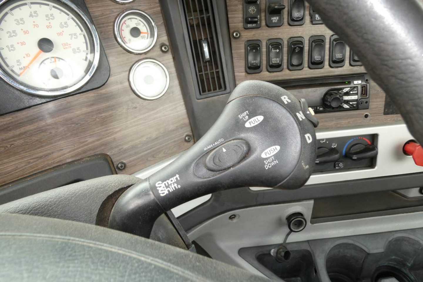 Truck interior showing steering column with gear selector, dashboard gauges, and woodgrain paneling.