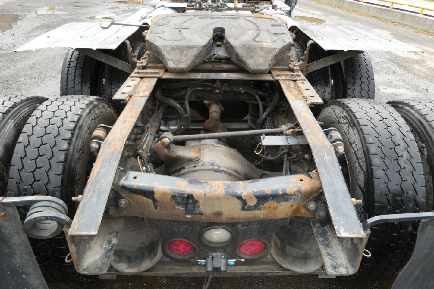 Rear view of a Freightliner SD122 chassis showing drivetrain, axles, and coupling—rusty frame with dual rear axles and fifth wheel area.