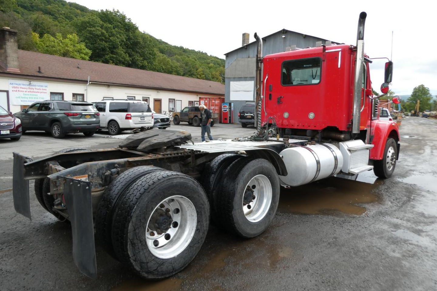 Truck chassis and cab view of a red Freightliner SD122 daycab with rear dual rear axles and fuel tanks, showing the side profile and bare frame.