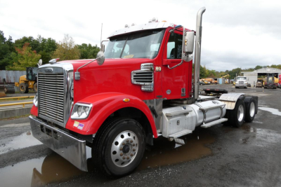 Freightliner SD122 conventional daycab tractor showing red cab, chrome grille, twin vertical exhaust stacks, front bumper, dual rear axles, and large fuel tanks.