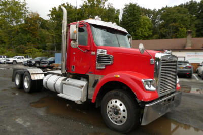 Red Freightliner SD122 daycab truck shown in side-angle view with chrome grille, dual rear axles, fuel tanks, and tall exhaust stacks.