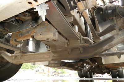 Conventional daycab truck undercarriage showing suspension components and driveline from passenger side perspective.