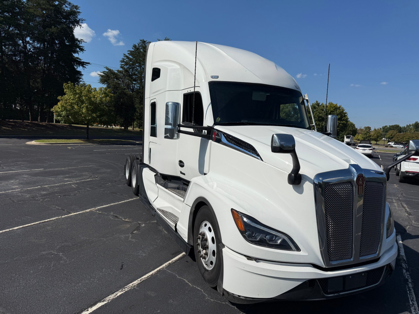 Kenworth T680 sleeper tractor in a parking lot, white cab with large chrome grille and aerodynamic mirrors, front-right view, VIN visible in listing.