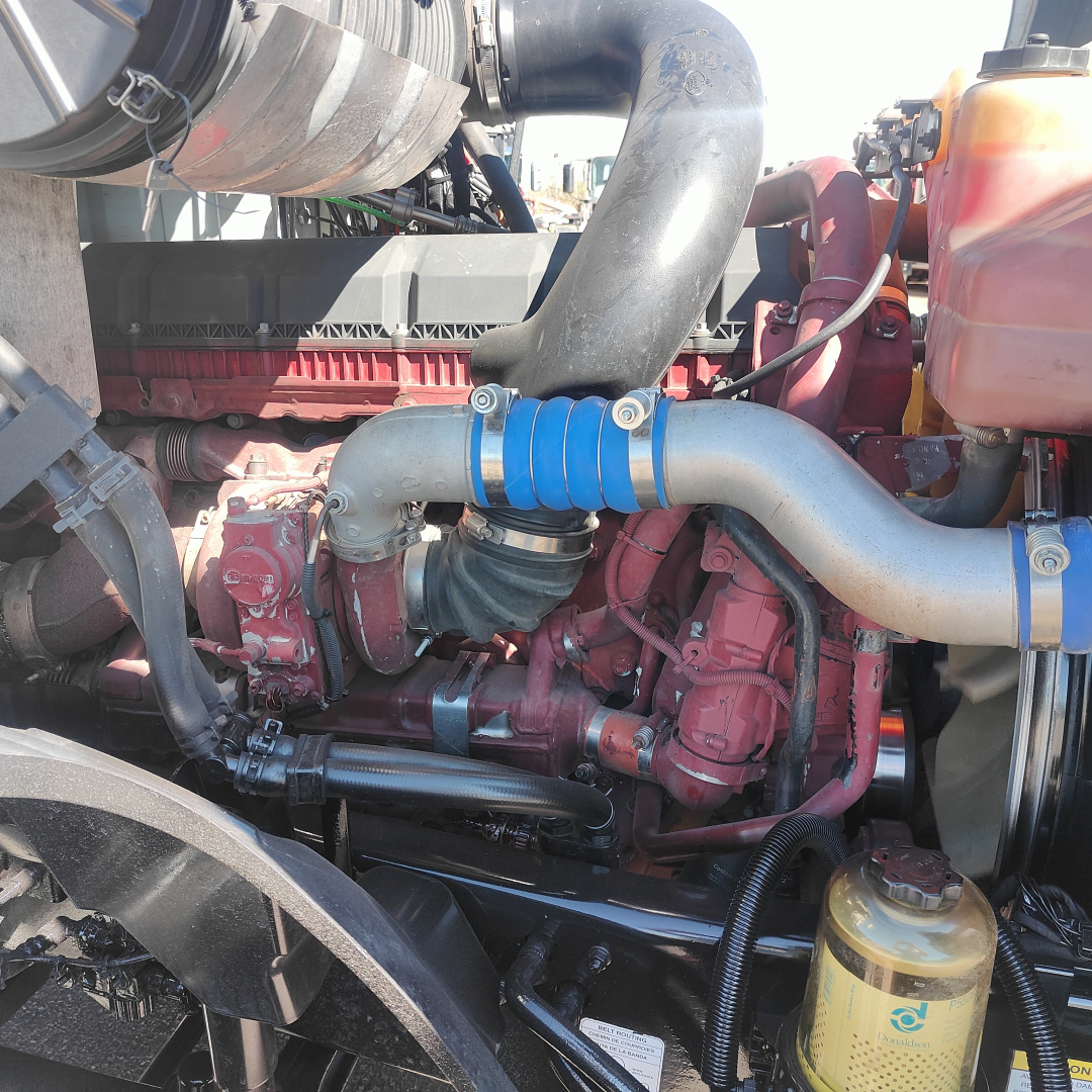 Engine bay of a 2019 Mack Anthem showing a red engine with blue silicone hoses, various metal pipes, black wiring, and a translucent coolant reservoir on the right.