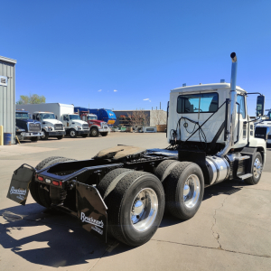 Truck tractor in a lot showing rear dual axles and mud flaps with brand stickers.