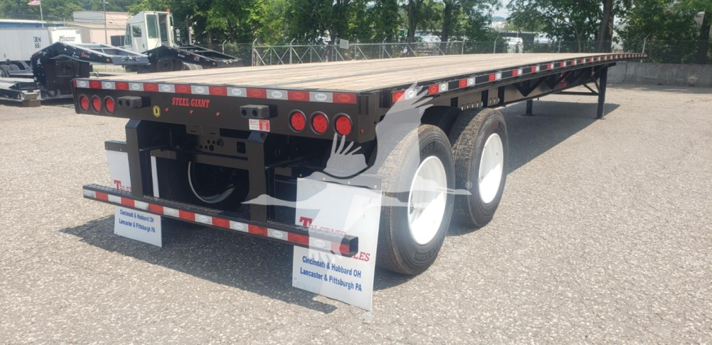 Flatbed trailer with tandem axles and dual rear wheels, long wood deck, rear lights, and sign decals.