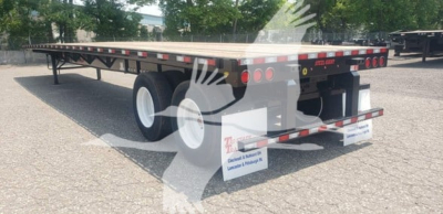 Flatbed trailer with tandem wheels and rear mud flaps showing DOT lights and reflective tape, viewed from rear-left angle.