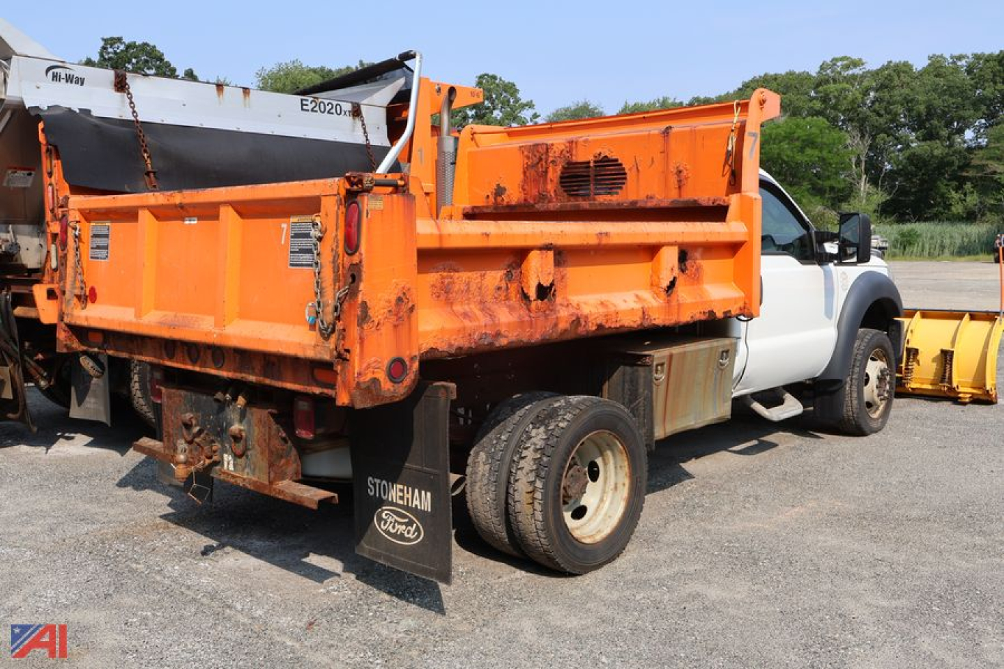 Orange dump bed on a white Ford F-550 pickup truck, side view showing dump body and plow equipment.