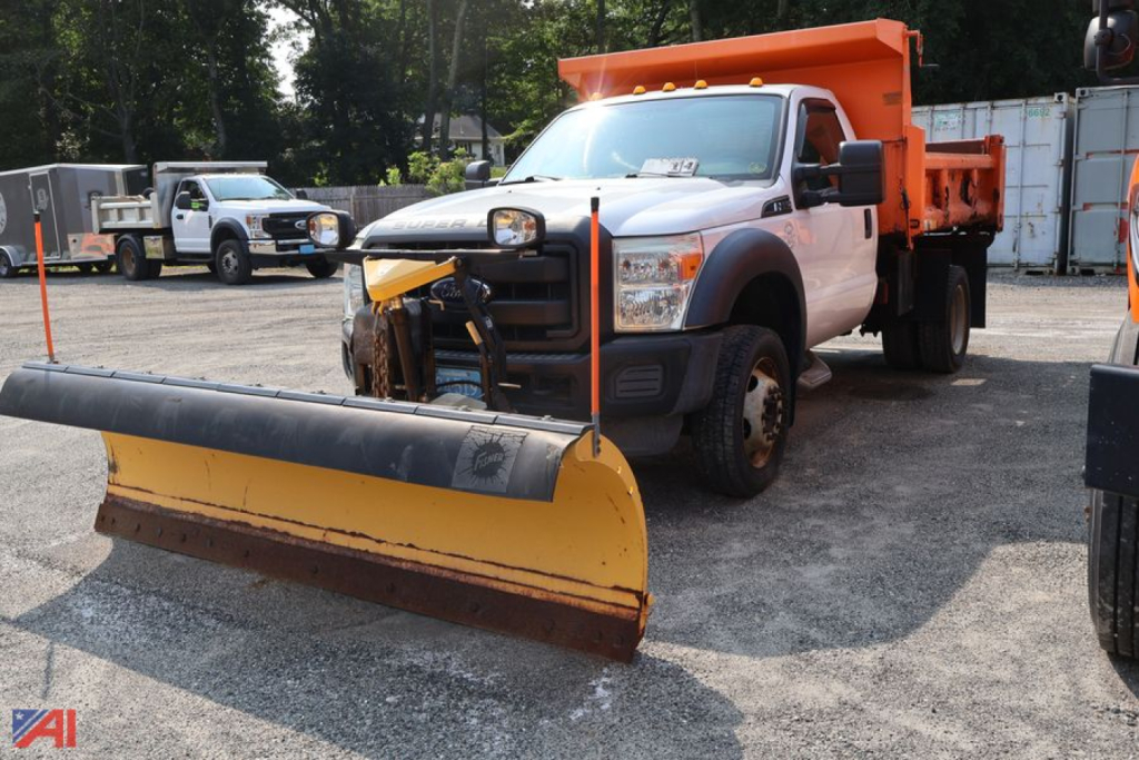 Ford F-550 dump truck with front plow and orange bed, in-service work vehicle, front view with snow plow attached.