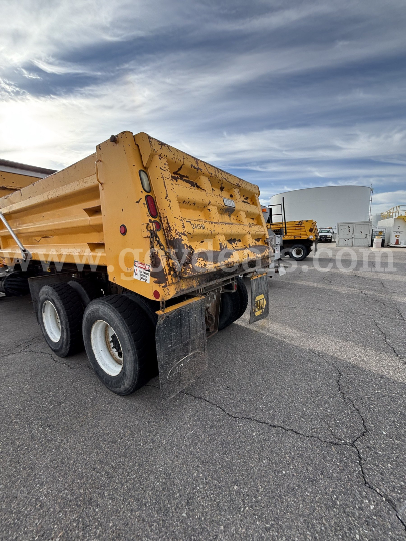 Rear view of a yellow Mack CV dump truck with a triple wheel configuration and black mud flaps.