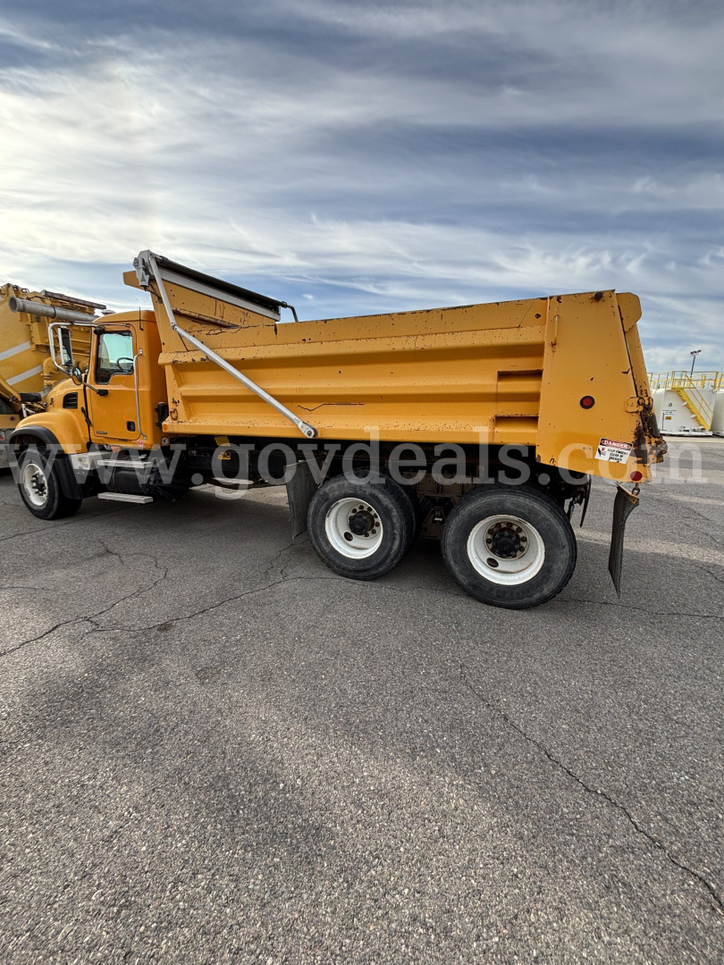 Mack CV (Granite) CV713 dump truck side view showing large orange dump bed with hydraulic hoist, dual rear axles and wheel wells.