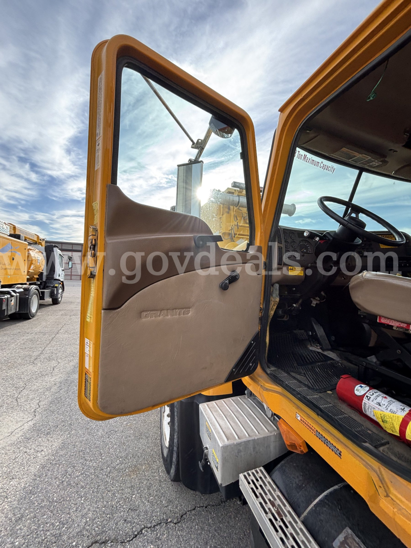Open driver door of a yellow Mack CV Granite dump truck showing interior and steps with dashboard visible.