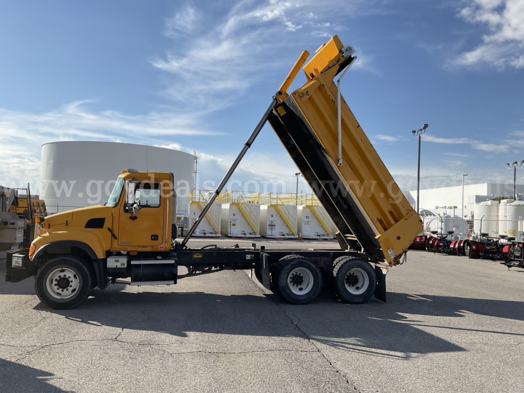 2003 Mack CV Granite dump truck in side profile with raised bed, yellow cab and black chassis, front and rear wheels visible, outdoor lot.