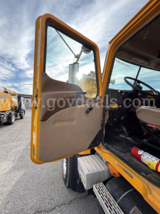 Open driver door of a yellow Mack CV Granite dump truck showing interior and steps with dashboard visible.