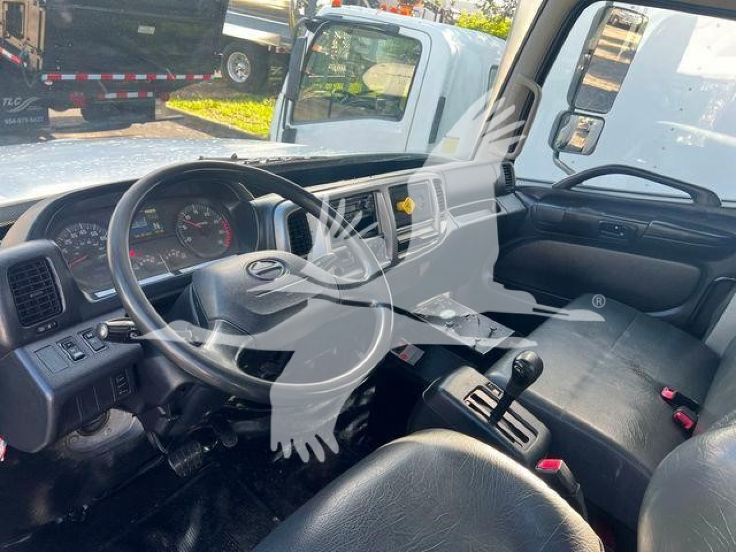 Cab interior of a 2019 Hino 338 toward the driver's seat with steering wheel, dashboard, and gear shifter visible.