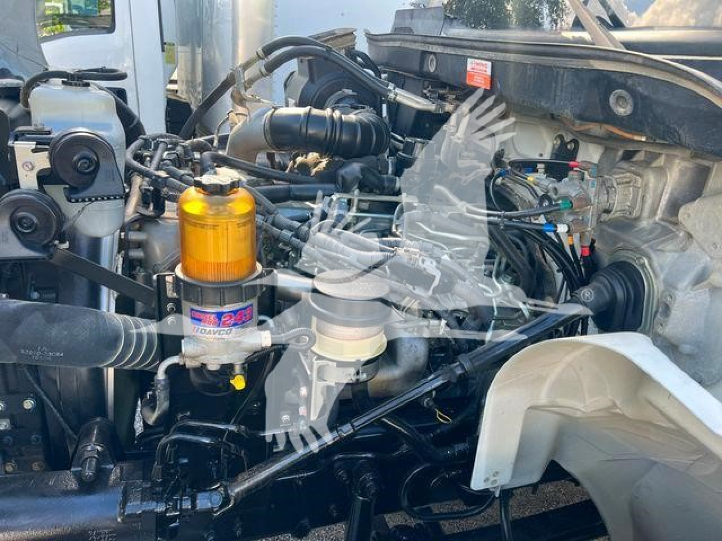 Trucks engine bay with visible filters and hoses; orange fuel/air separator canister labeled Volvo (brand) and various black hoses, metal piping, and battery area in view.