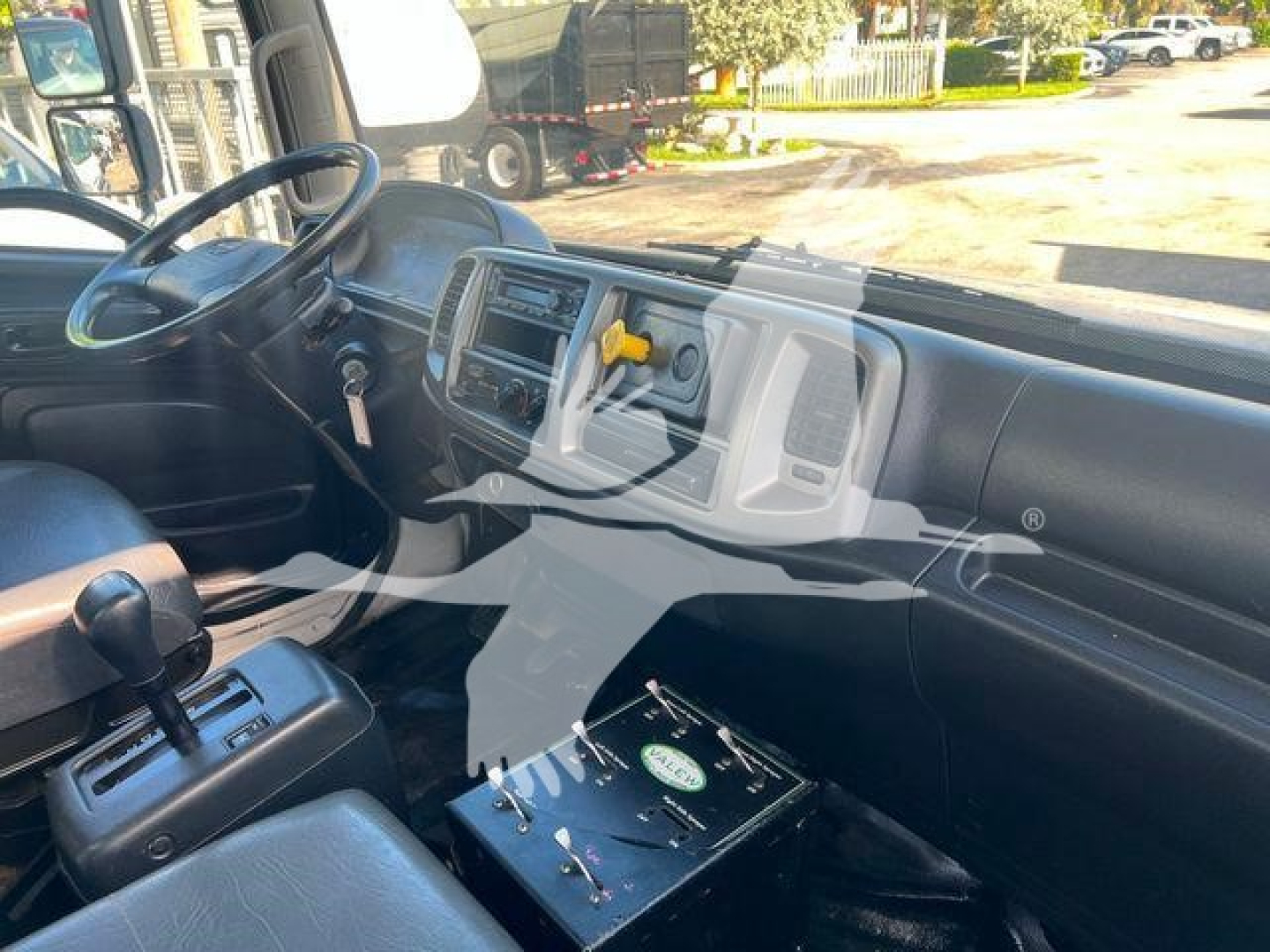 Interior of a 2019 Hino 338 cab showing steering wheel, dashboard with center console, gear selector on floor, and a black battery box on the passenger side.