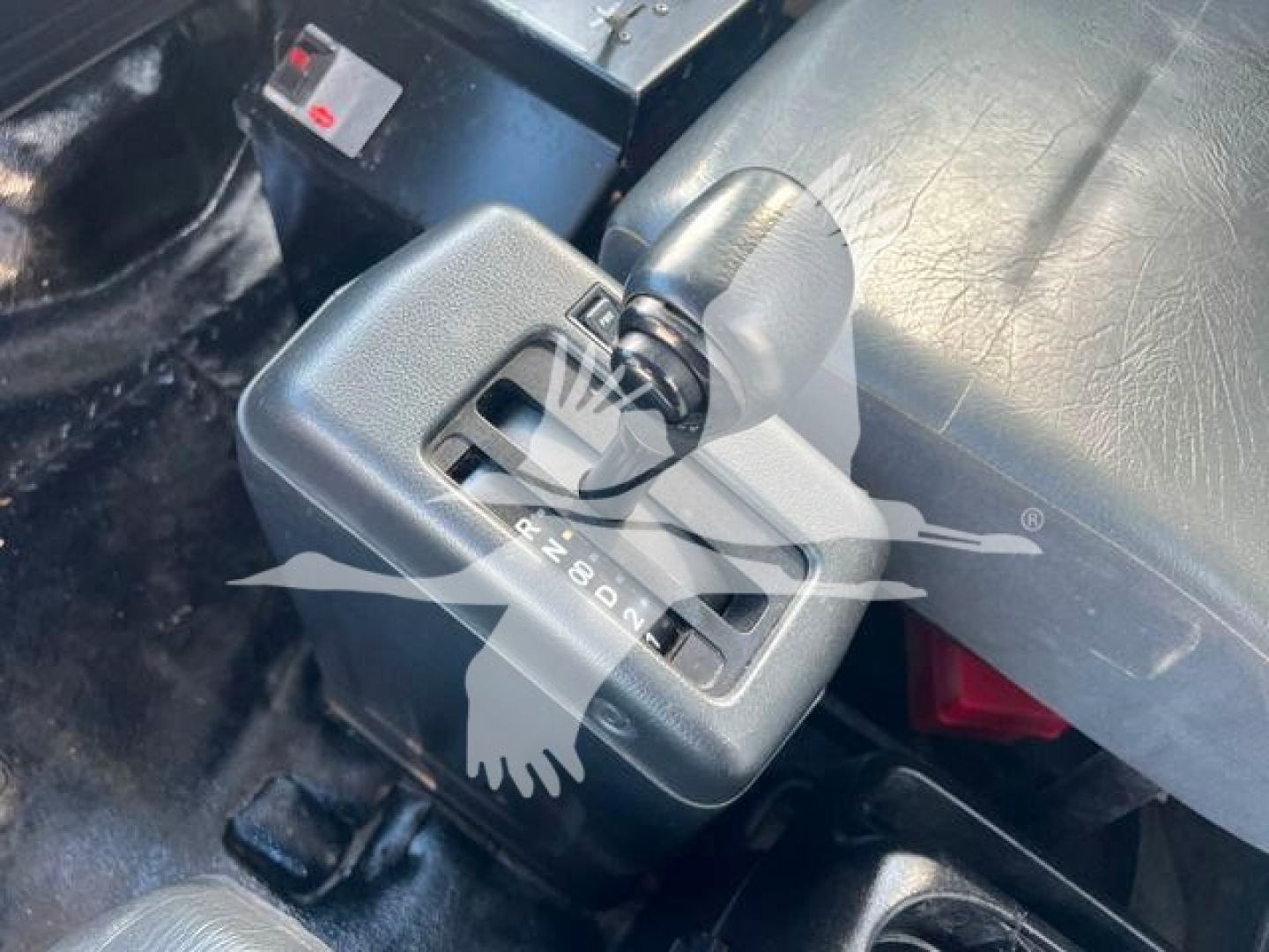 Gear shifter with visible indicator showing PRNDL on a Hino dashboard. Partial view of surrounding console and wiring.