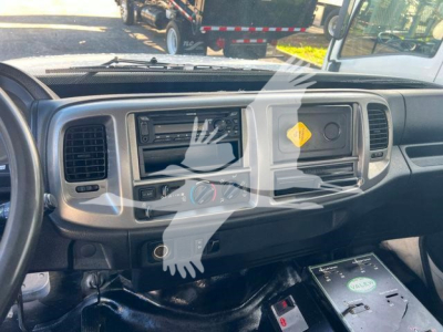 Cab interior of a 2019 Hino 338 showing dashboard with steering column, center console, radio, climate controls, and a yellow hazard placard on the passenger side; visible gear area and a control module.
