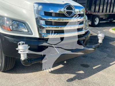 Front of a white 2019 Hino 338 truck with a chrome grille and bumper, showing a distinctive front hitch setup and dual tow hooks on a black bumper, parked outdoors.