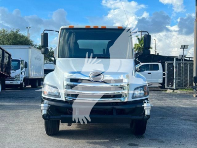 White 2019 Hino 338 front view with Hino emblem, large grille, headlights, and side mirrors; orange clearance lights on roof; reflection of sky.