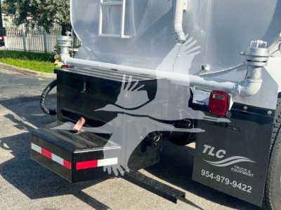 Rear view of a 2019 Hino 338 dump truck showing a black underbody toolbox with a red reflective stripe, TLC decals, and contact number, plus tail light and hydraulic piping.