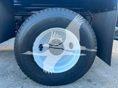 Wheel and tire assembly of a 2019 Hino 338 front wheel with white steel rim and black tire, visible fender and partial undercarriage.