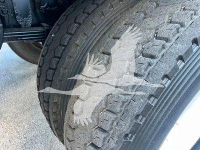 Truck front wheel well with large treaded tire and part of suspension; no legible labels or text visible.