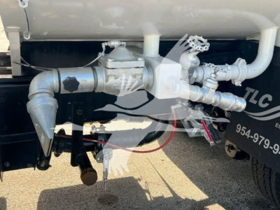 Hino 338 truck fuel/water system undercarriage showing piping, valves, and a spray nozzle. Visible metal pipes, fittings, and a valve handle with hoses.